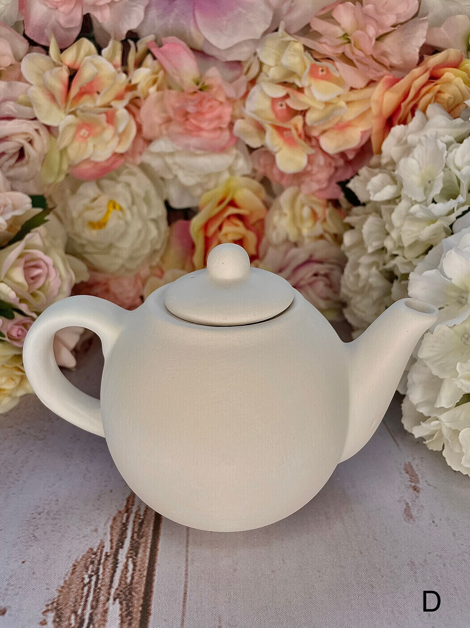 A white teapot is sitting in front of a bunch of flowers