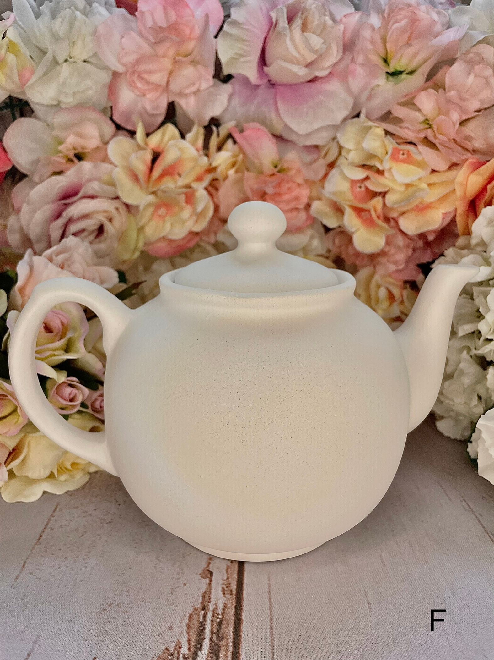 A white teapot is sitting in front of a bunch of pink flowers