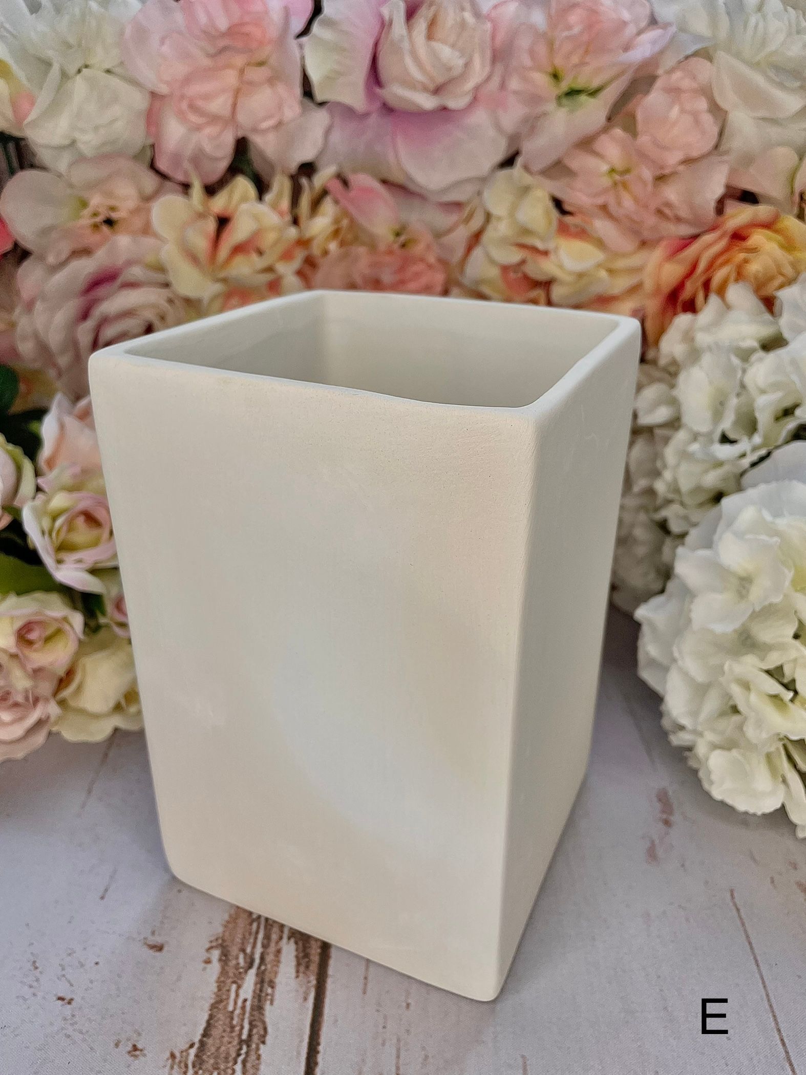 A white vase is sitting on a wooden table next to flowers.