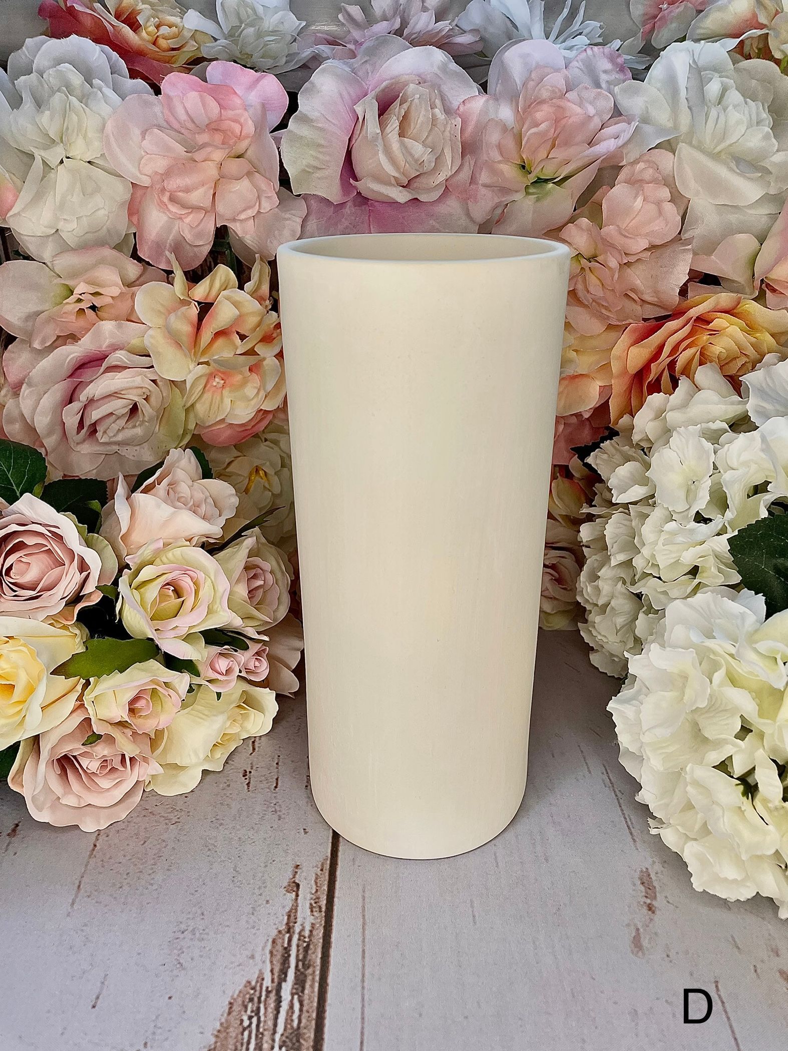 A white candle is sitting on a wooden table surrounded by flowers.