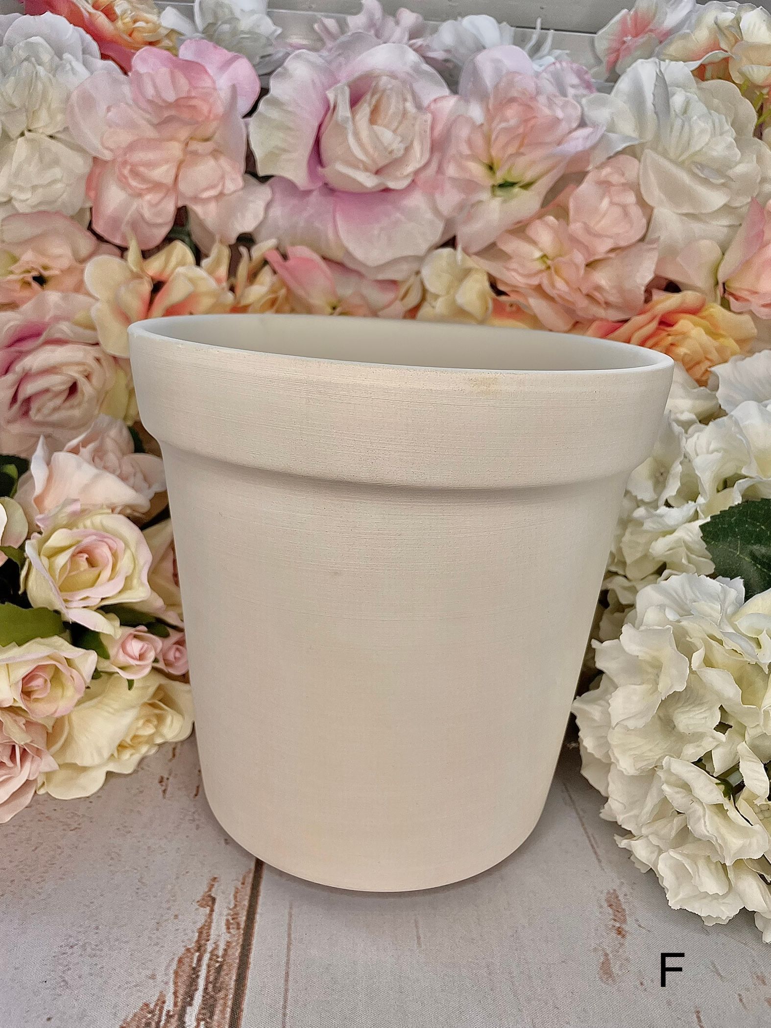 A white pot is sitting on a table next to flowers.