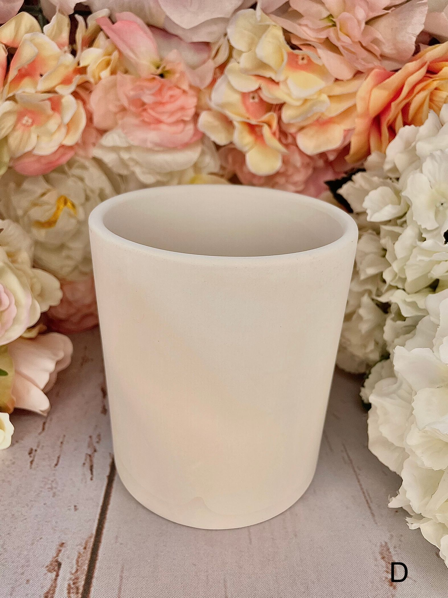 A white cup is sitting on a wooden table next to flowers.