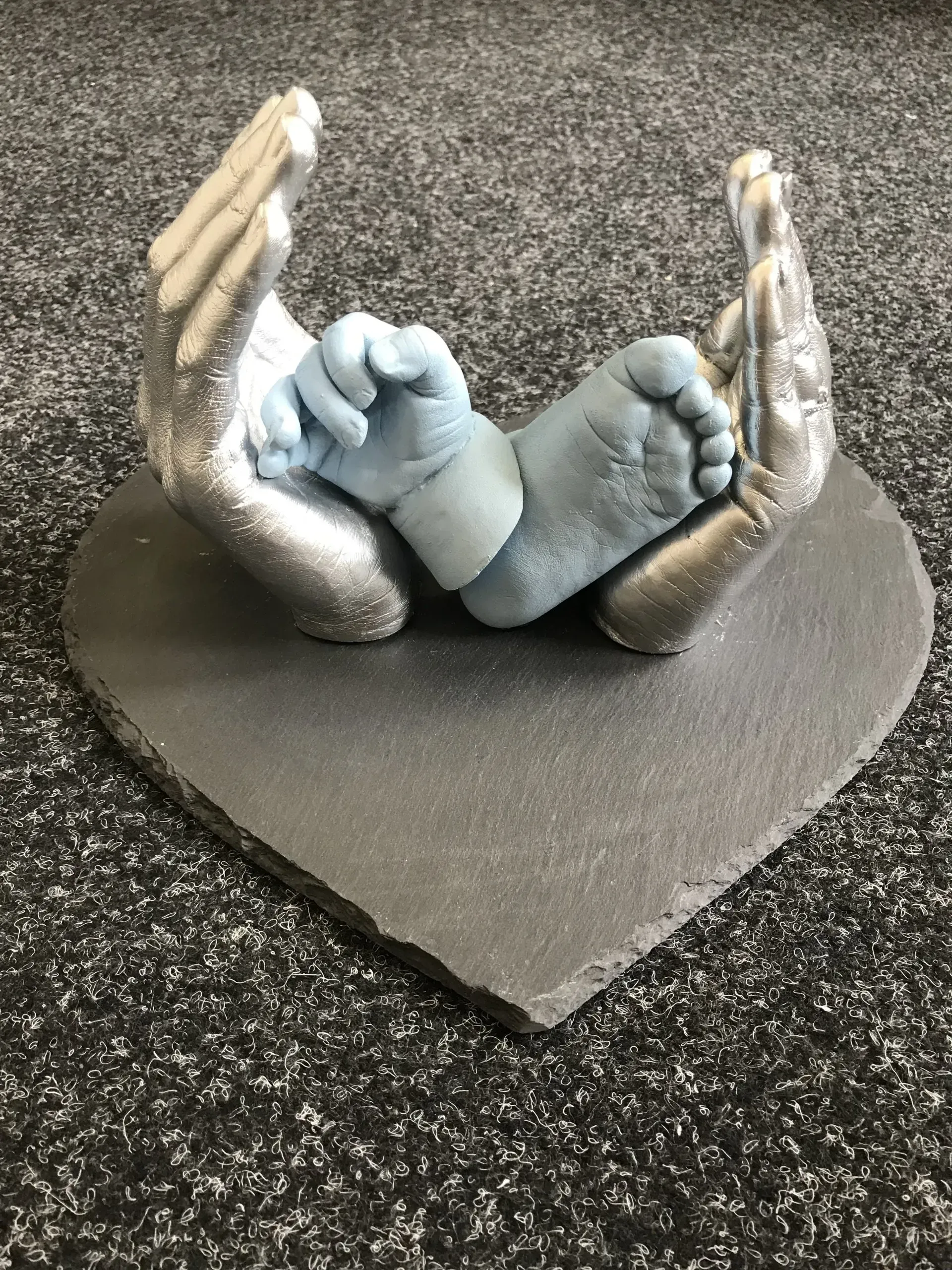 A statue of a baby 's hands and feet on a heart shaped plate.
