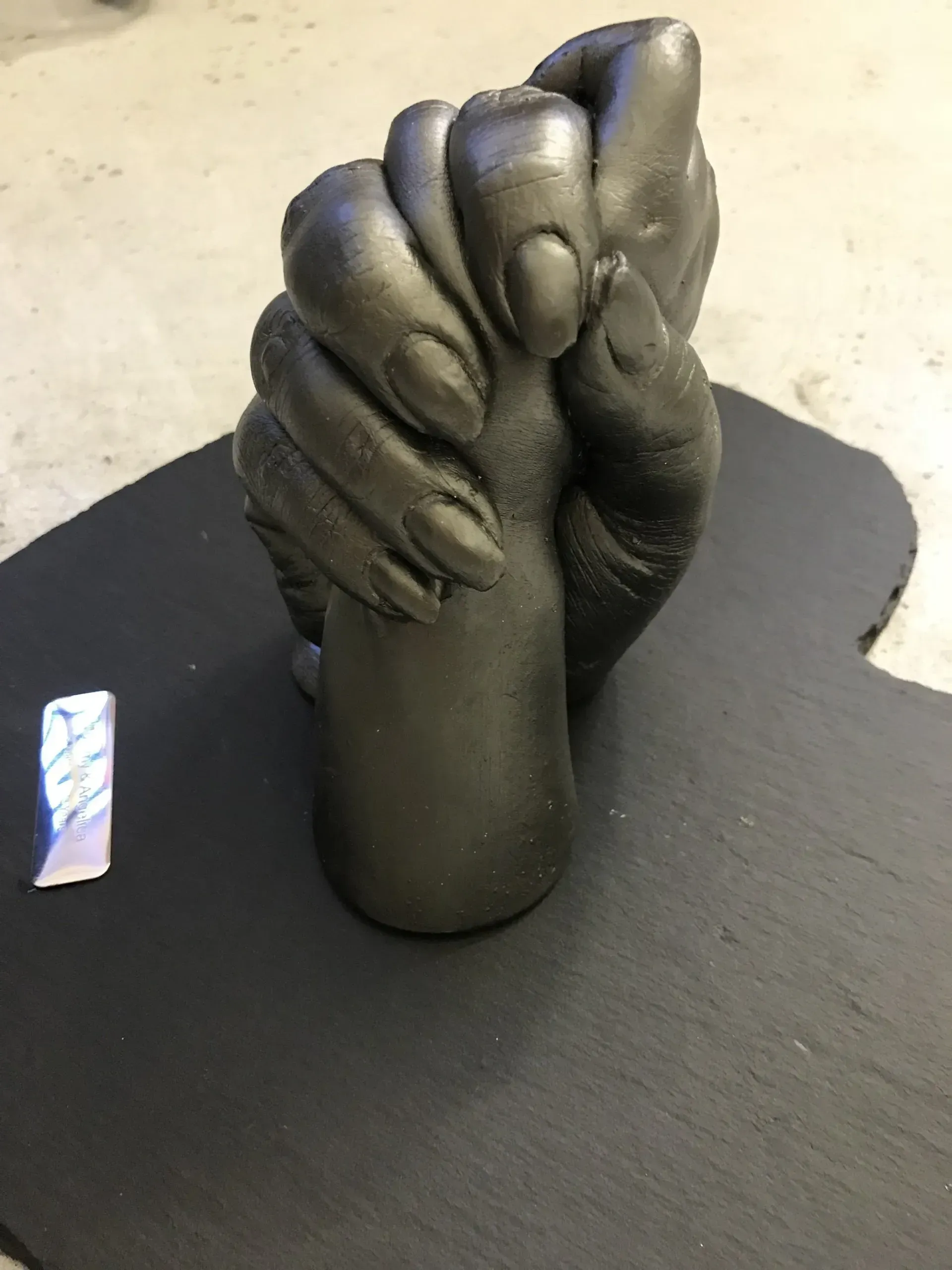 A statue of two hands holding each other on a black surface.