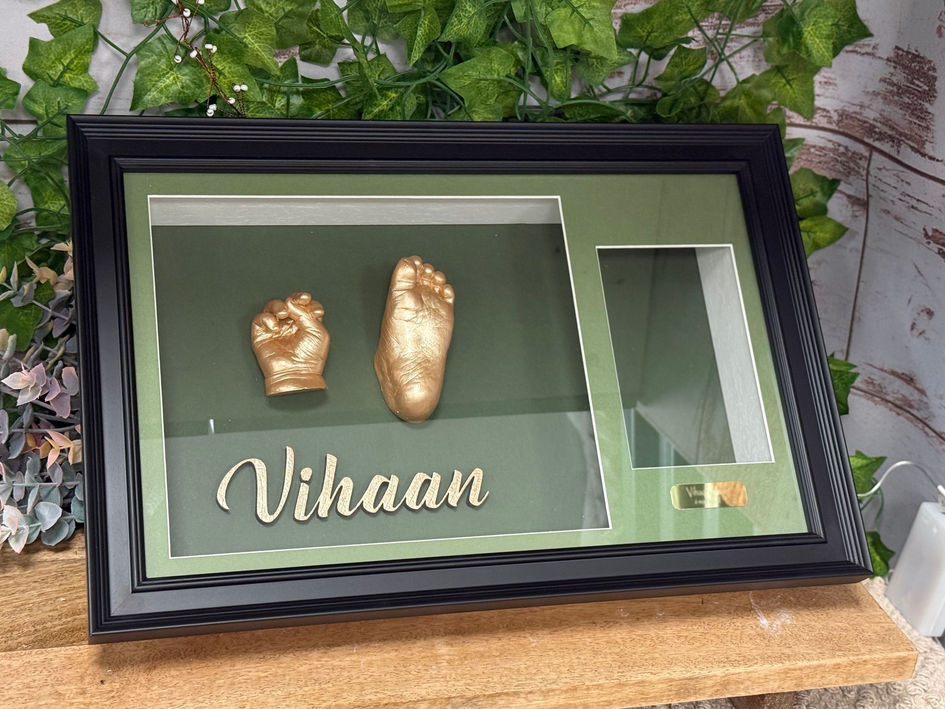 A framed keepsake with gold-painted baby hand and foot casts, name