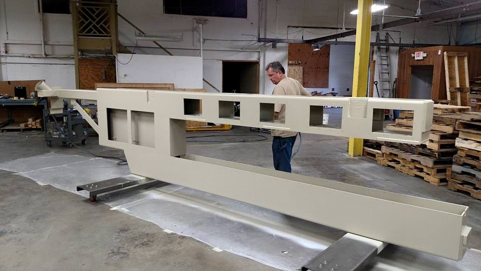 Man inspecting large, beige industrial metal structure with rectangular cutouts in a factory setting.