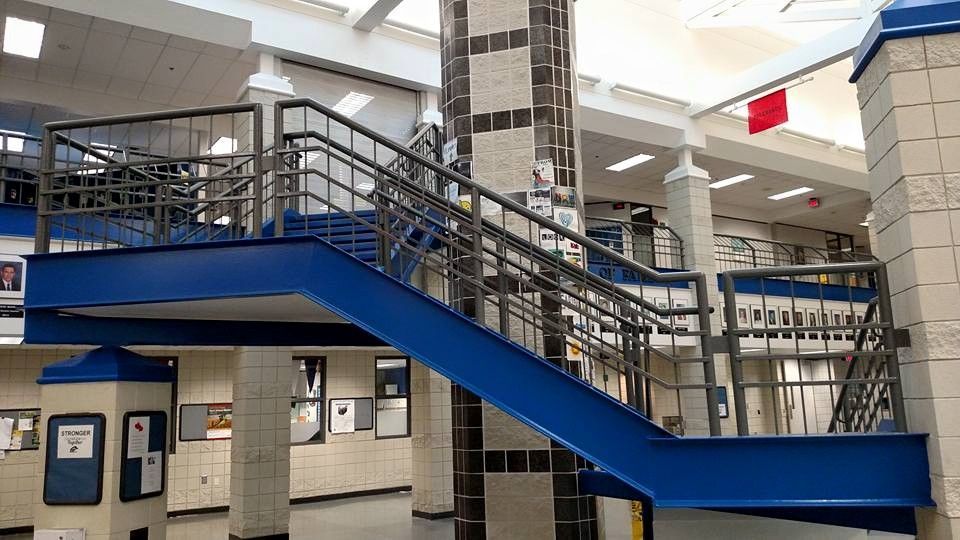 Blue and gray staircase in a school hallway with a tile pillar and framed displays.