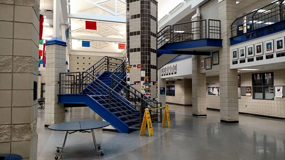 Interior of a school hallway with blue staircases, a large pillar, and flags hanging from the ceiling.