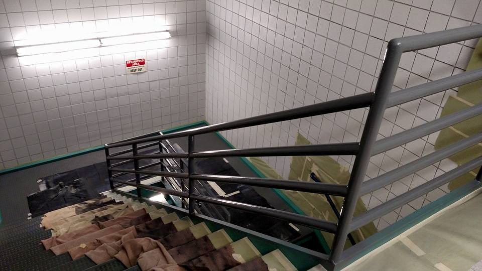 Stairwell with metal handrails; tiled walls and brick stairs lead downward.