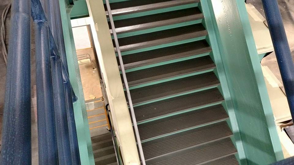 Metal staircase with green railing and non-slip treads, viewed from above.