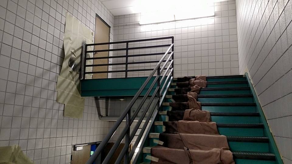 Stairwell with teal steps, black railing, and white tile walls. Insulation hangs on the left.