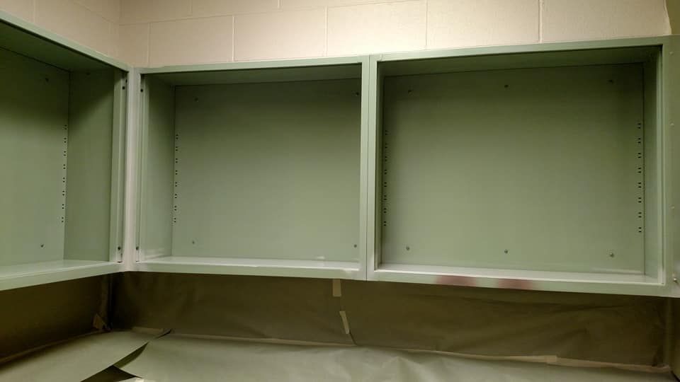 Three light green open wall cabinets, freshly painted, with taped-off floor and wall above.