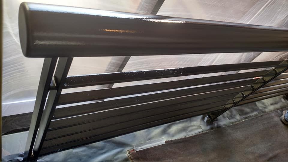 Dark gray metal bench in a greenhouse setting.