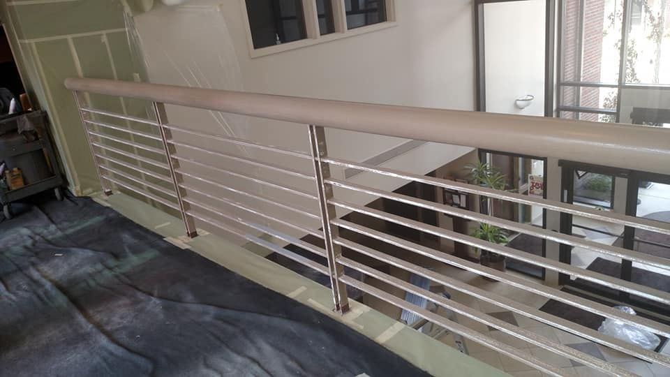 Interior view of a balcony railing made of horizontal silver bars and a beige handrail.