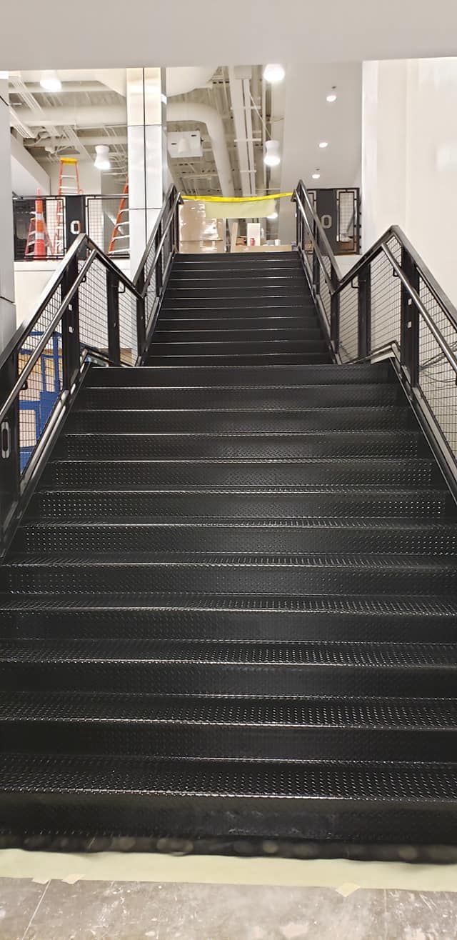 Staircase with black metal steps and handrails leading upwards inside a building.