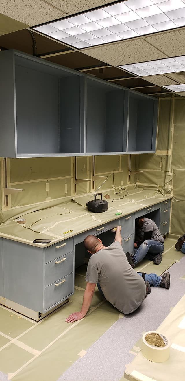 Two men installing cabinetry in a room with exposed insulation. Cabinets are gray.
