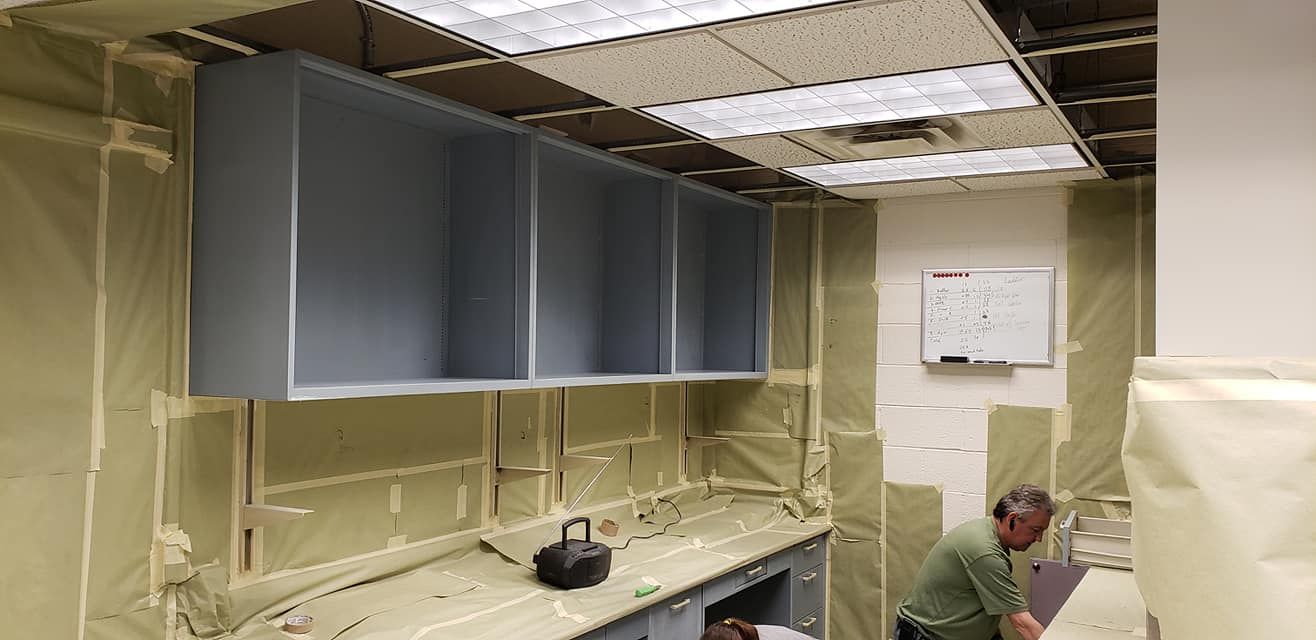 Room under construction with gray cabinets, exposed insulation, and a person working.