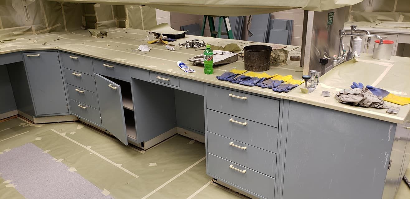 A cluttered gray lab countertop with cabinets and open cabinets, showing construction debris and tools.