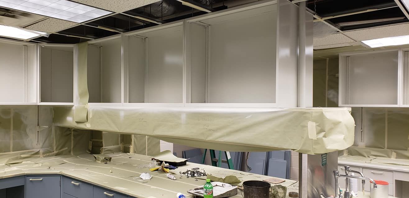 Laboratory cabinets and fume hood under construction, with masking tape and ceiling tiles visible.