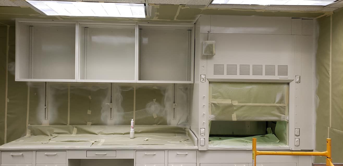 White cabinets in a lab setting, with a fume hood and open shelving.