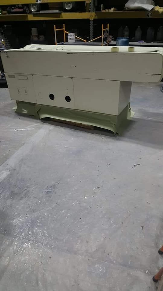 A large, beige industrial machine base on a gray tarp in a workshop.