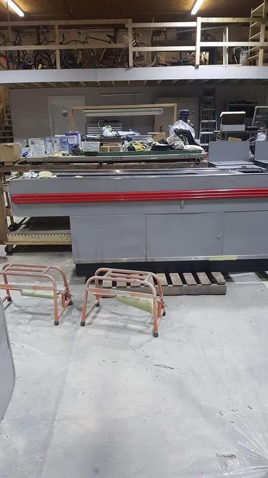 A large grey industrial machine with a red stripe sits in a workshop, with two orange rolling supports in the foreground.