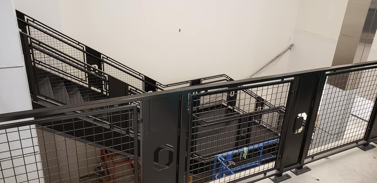 Staircase with black metal railings and a wire mesh design, angled downward from a higher level.