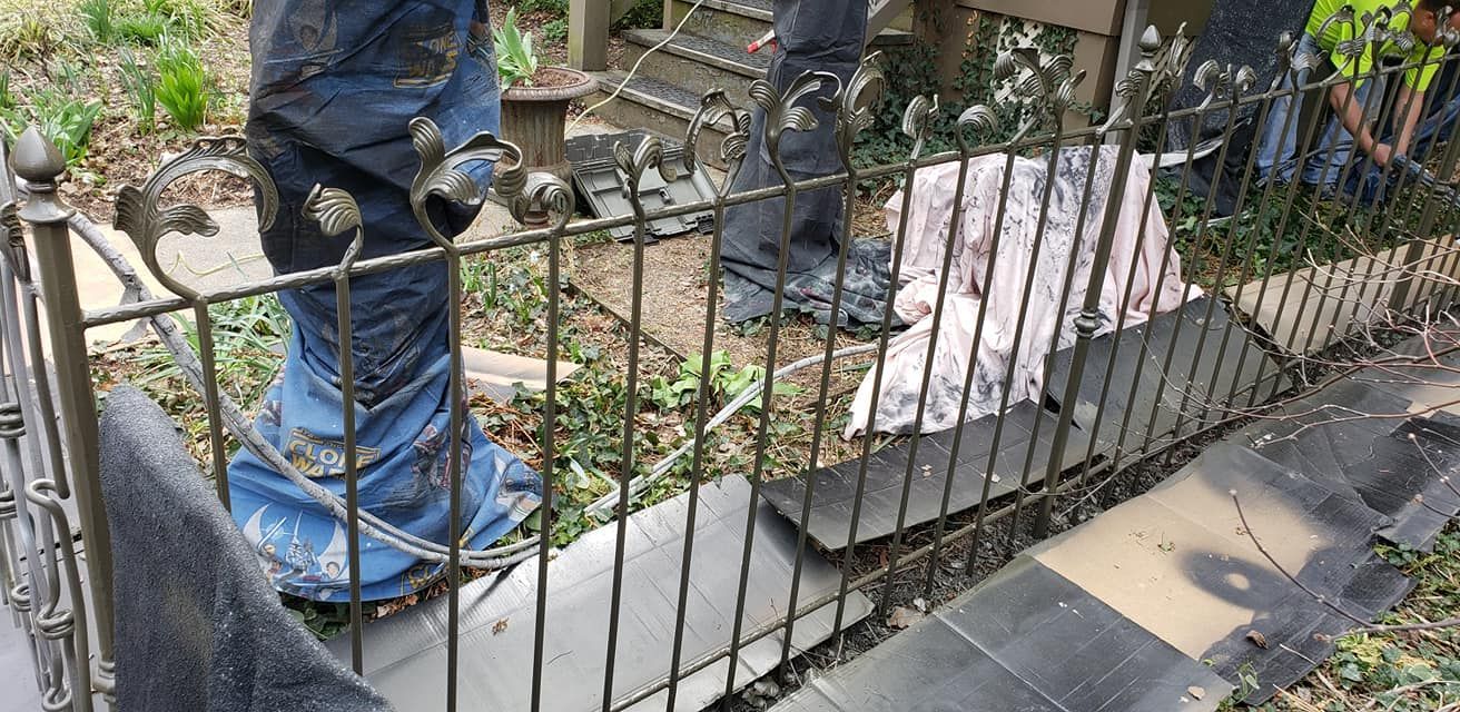 Person in blue jeans behind a decorative iron fence, with garden materials visible.