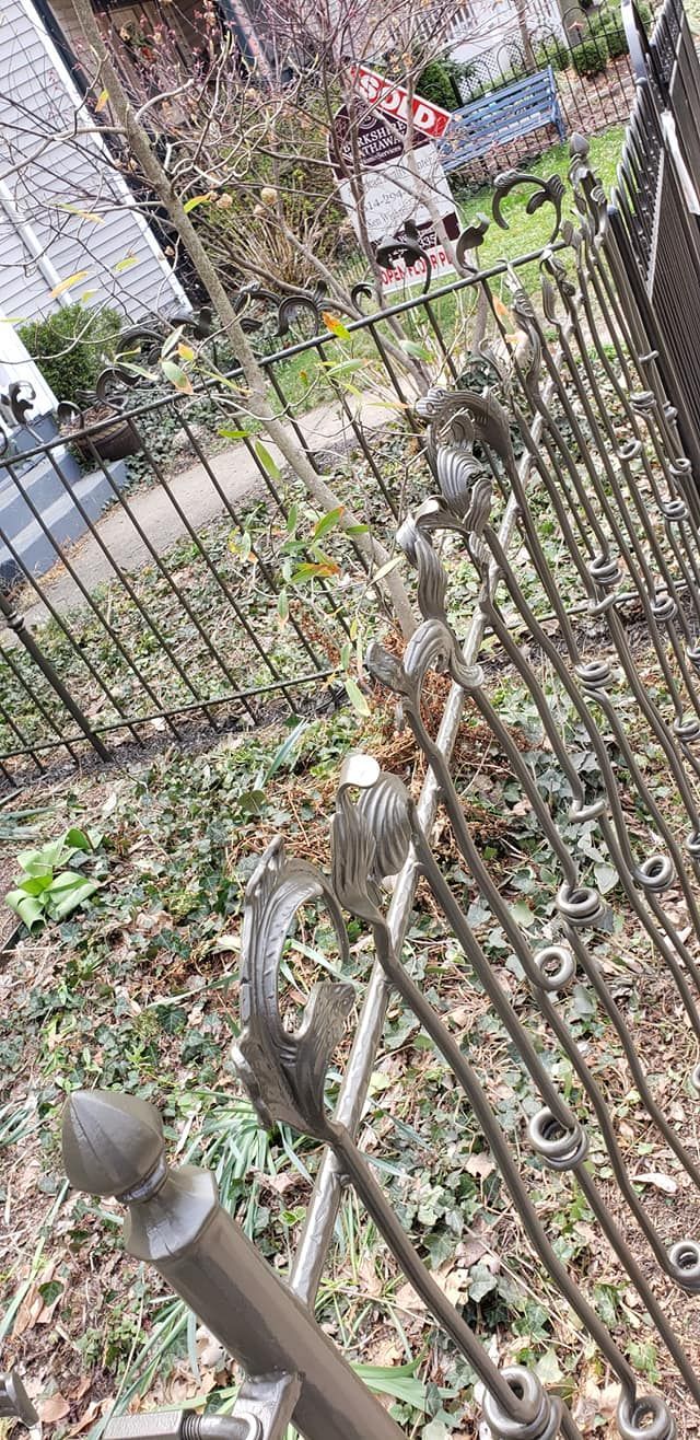 Iron fence with decorative scrollwork detail. Brown/gray tones, outdoors.