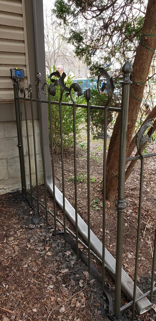 A wrought iron fence with decorative fleur-de-lis, next to a tree and wood chips.
