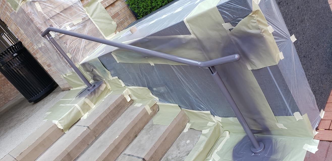 Handrail being painted, covered with plastic and tape. Steps and brick in the foreground.