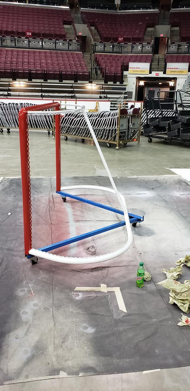 Hockey net in an arena, with red posts and blue base. White pipe forms the net.