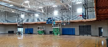 A gymnasium with basketball hoops, a wood floor, and blue wall pads.