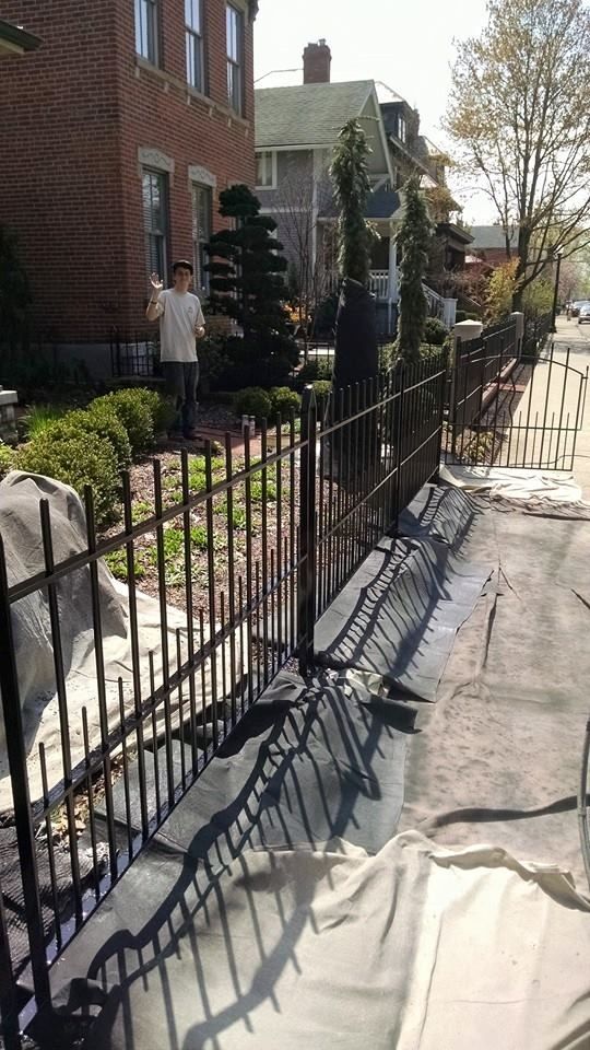 Black metal fence bordering a residential property with workers, greenery, and a brick house.