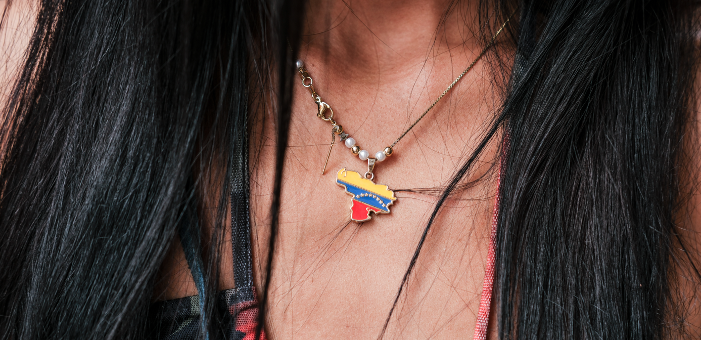 Primer plano de un collar de oro con un colgante colorido que descansa sobre cabello y piel oscuros.