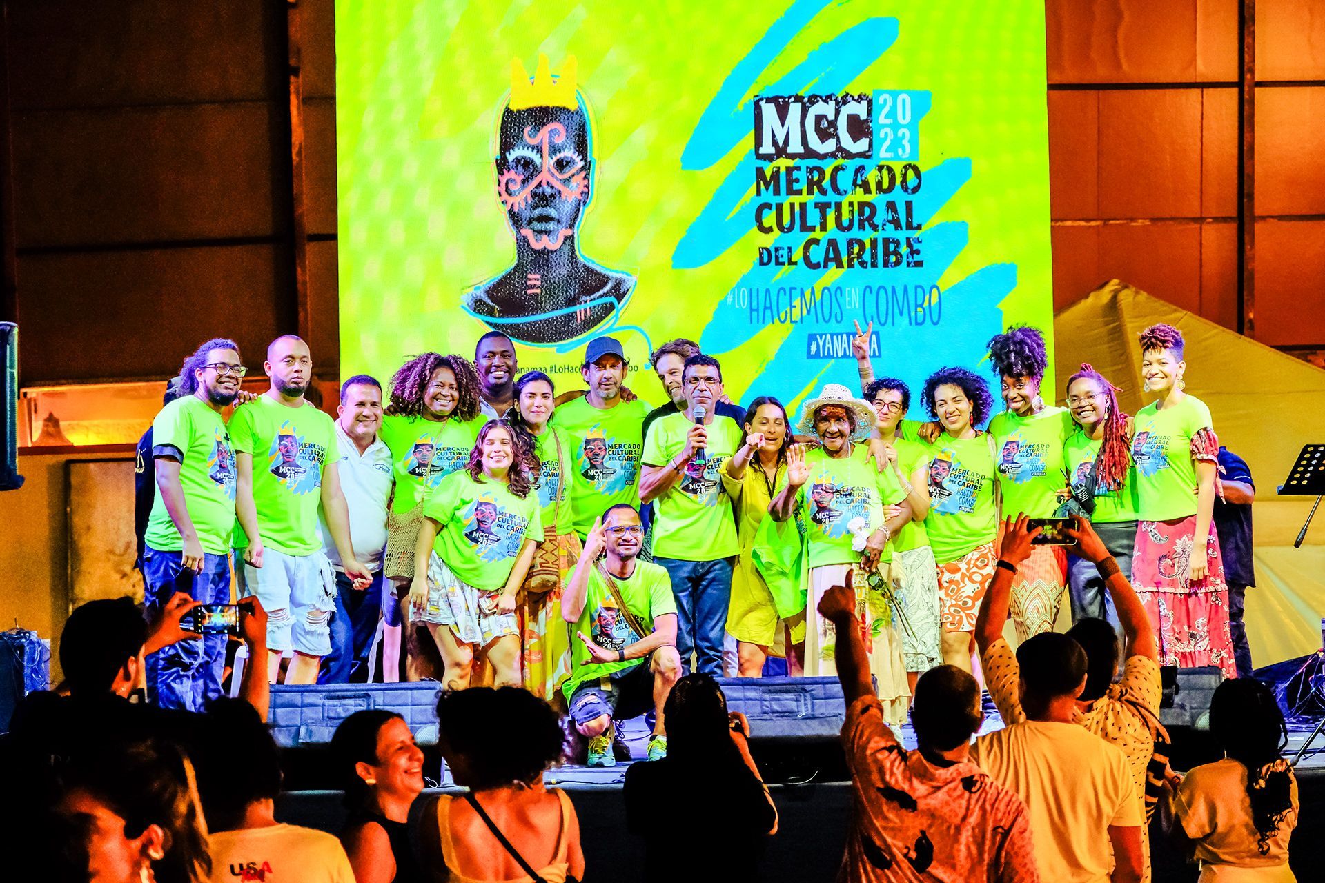 Grupo de personas en el escenario con camisetas llamativas en un evento cultural