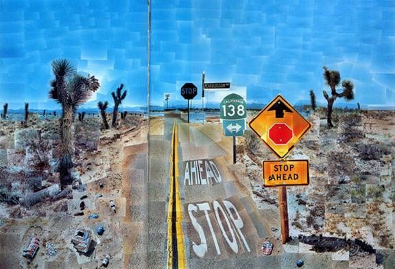 Carretera desértica con señales de stop, una señal de tráfico y árboles dispersos bajo un cielo azul brillante.