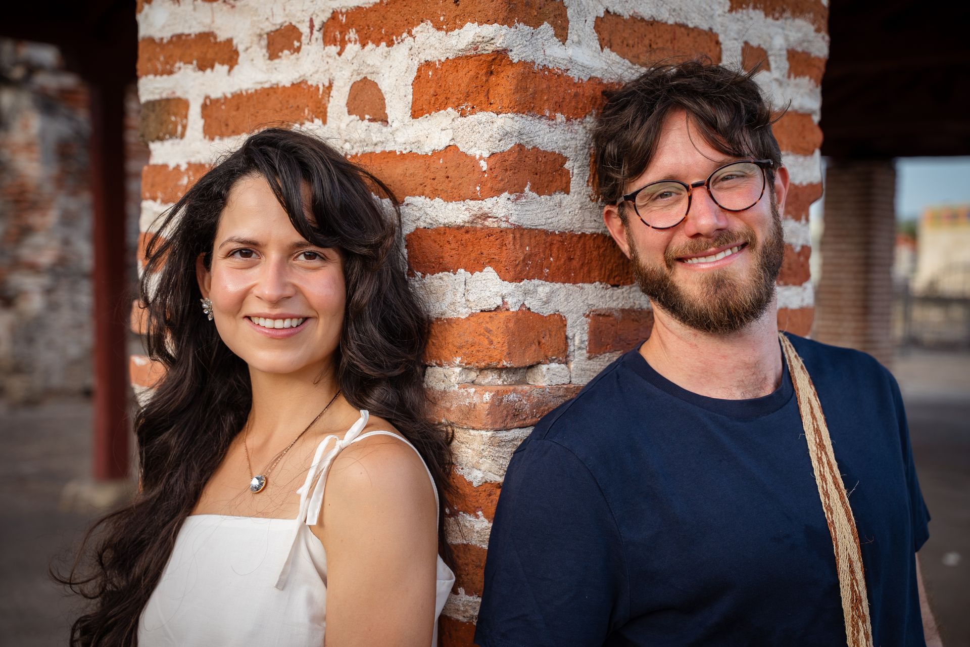 Dos personas sonrientes de pie junto a una pared de ladrillos
