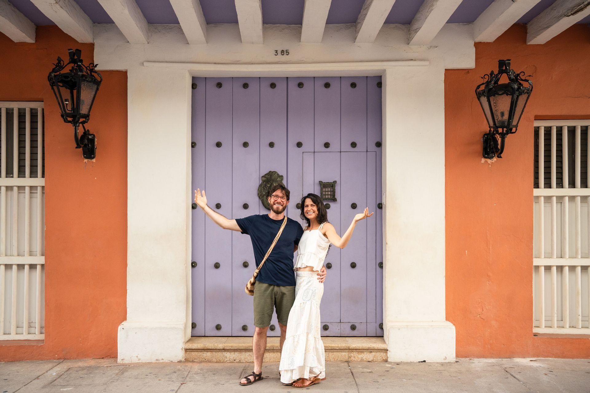 Dos personas posan frente a una puerta color lavanda y una pared color melocotón.