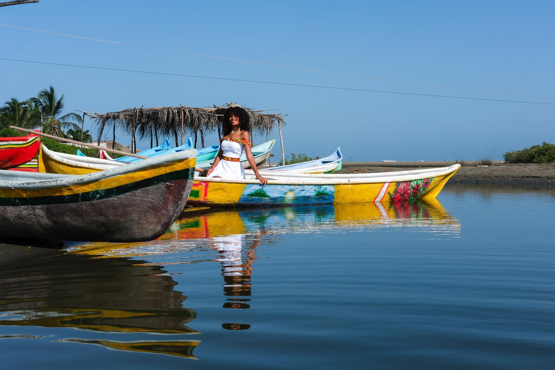 Barcos coloridos flotando en aguas azules y tranquilas, con una persona sentada en uno de ellos bajo un cielo despejado.