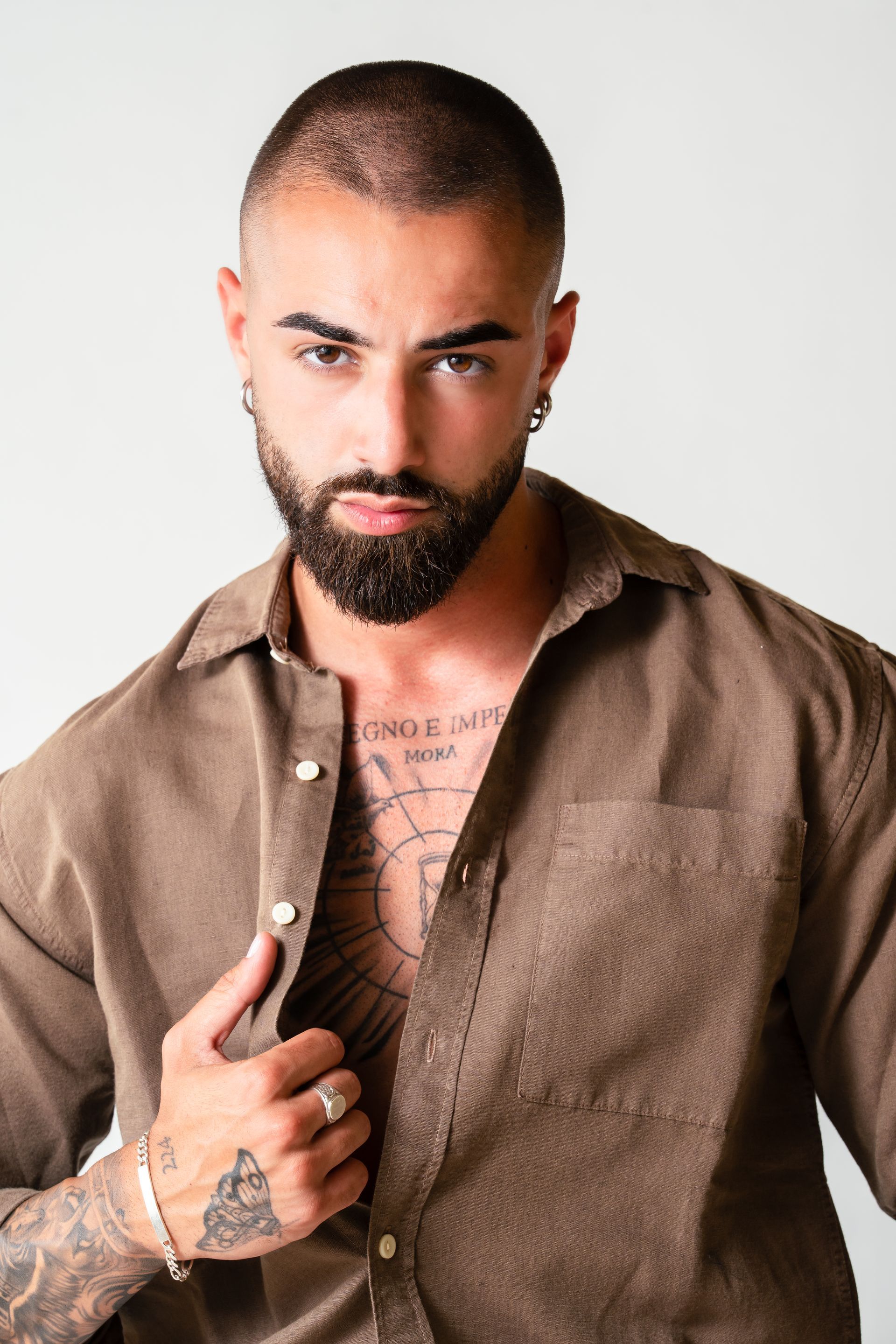 Hombre barbudo con camisa marrón posando contra un fondo claro.