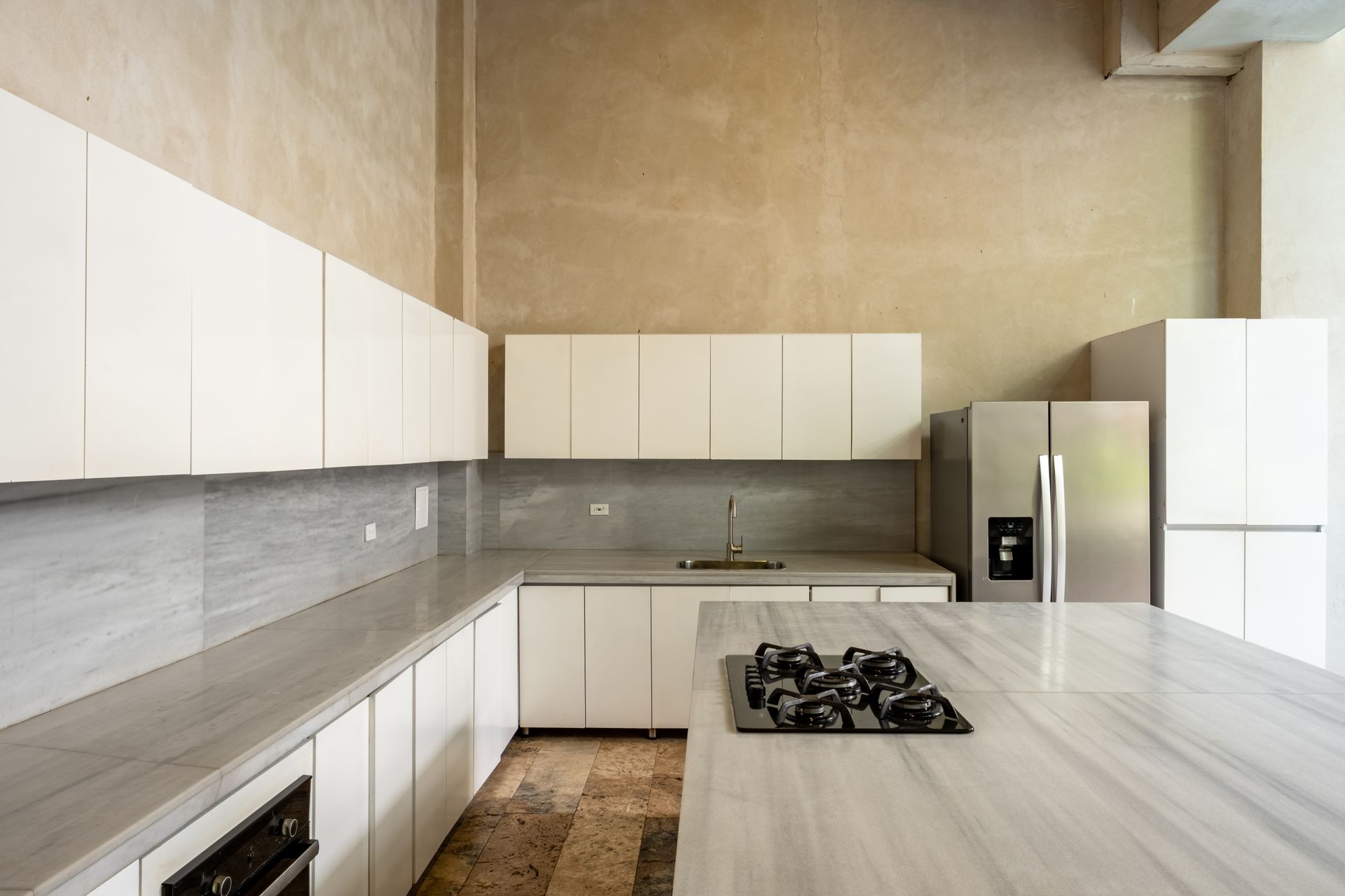 Cocina moderna minimalista con gabinetes blancos, encimeras grises y electrodomésticos de acero inoxidable.