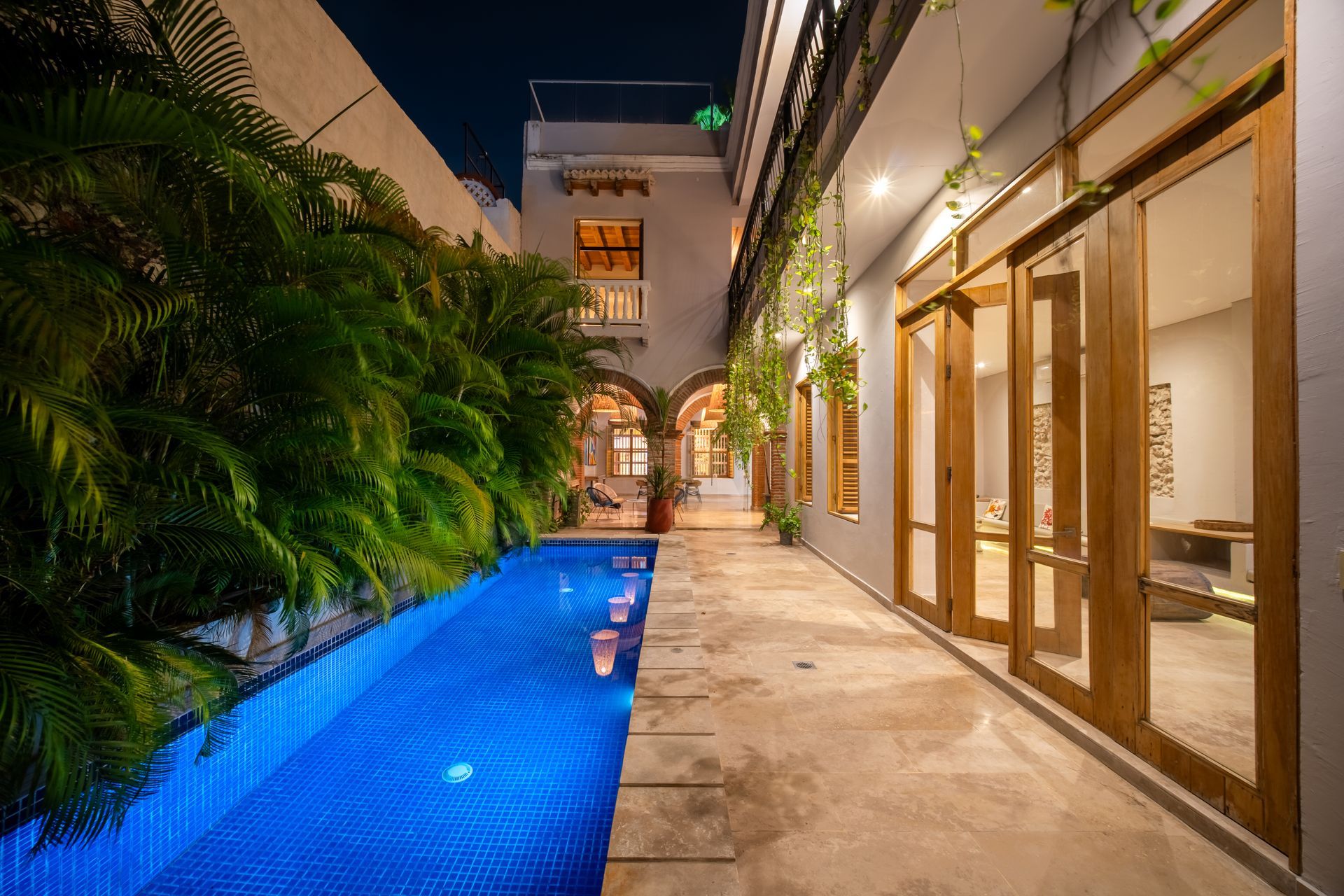 Estrecha piscina iluminada de azul junto al patio de una villa por la noche