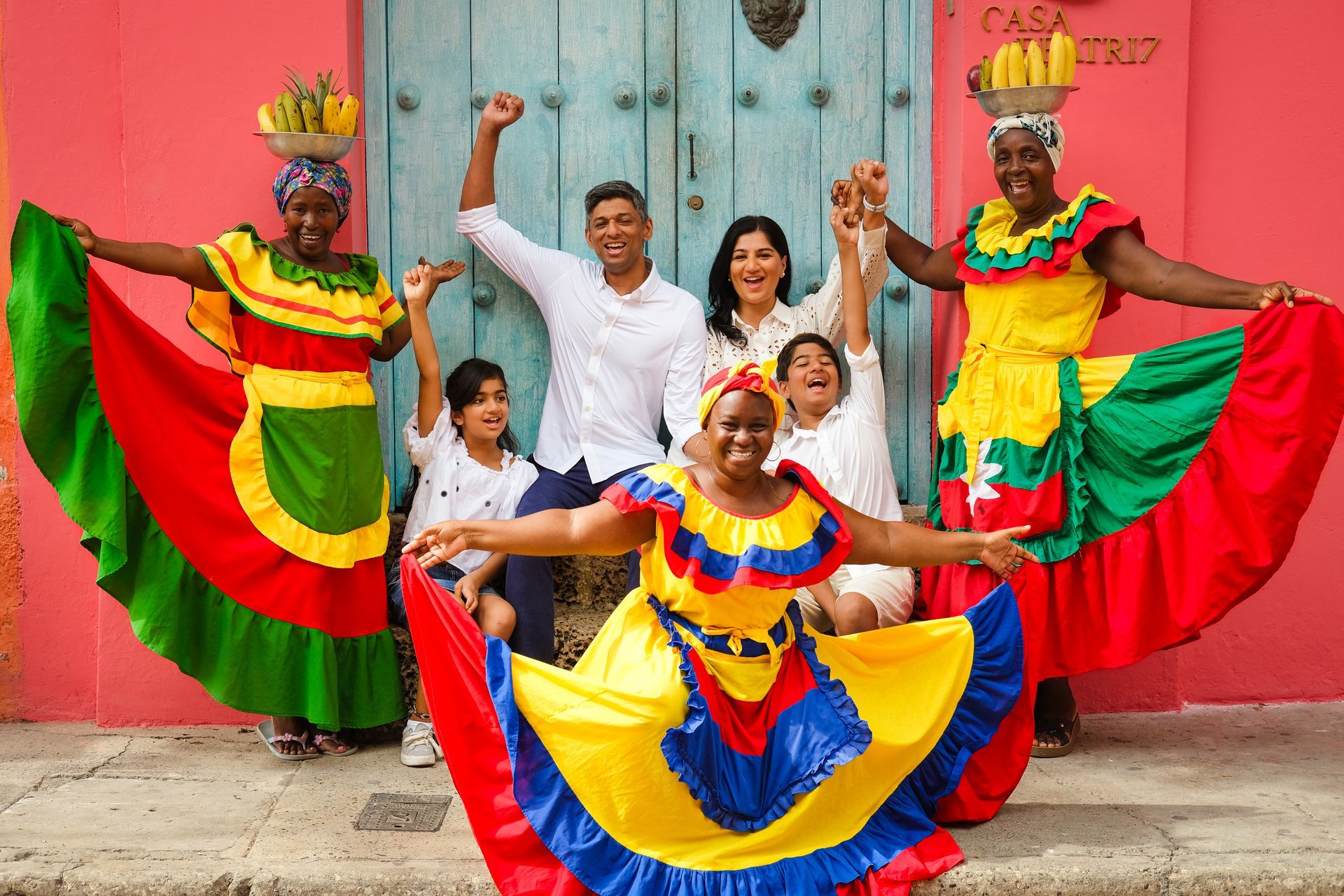 Bailarines tradicionales con coloridos trajes posando con los brazos en alto frente a una pared rosa.