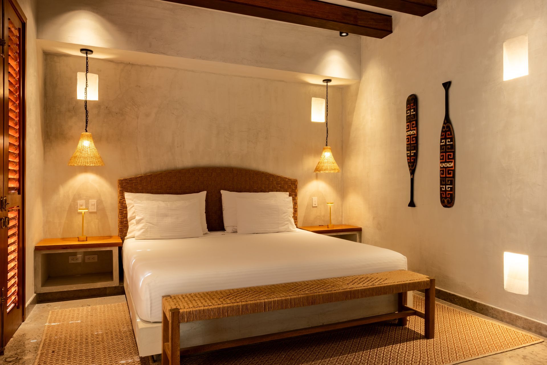 Acogedor dormitorio con cama de madera, apliques de pared cálidos y decoración tejida en una habitación de color beige.