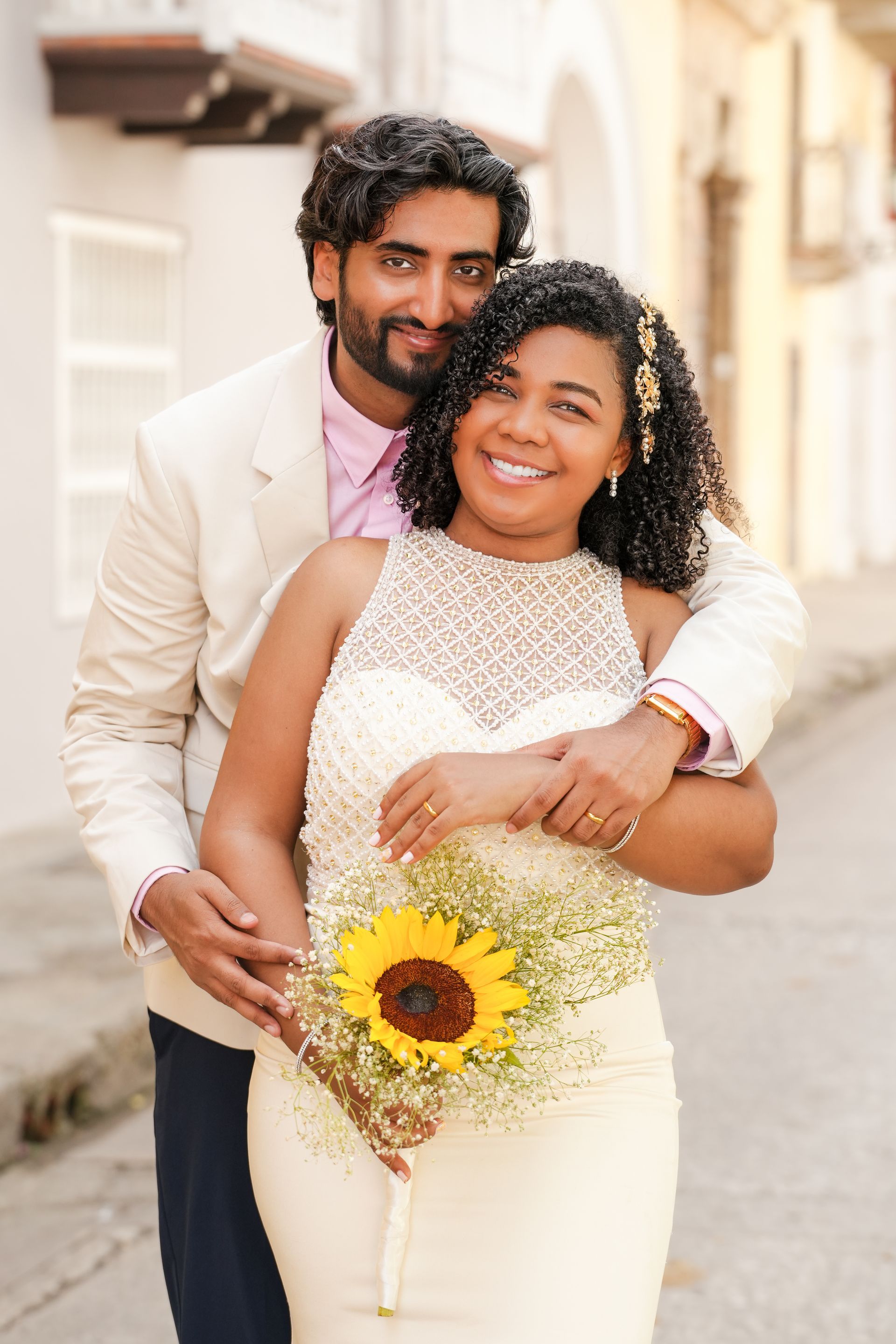 Pareja posando en una calle soleada de cartagena, sonriendo y sosteniendo un ramo de girasoles.