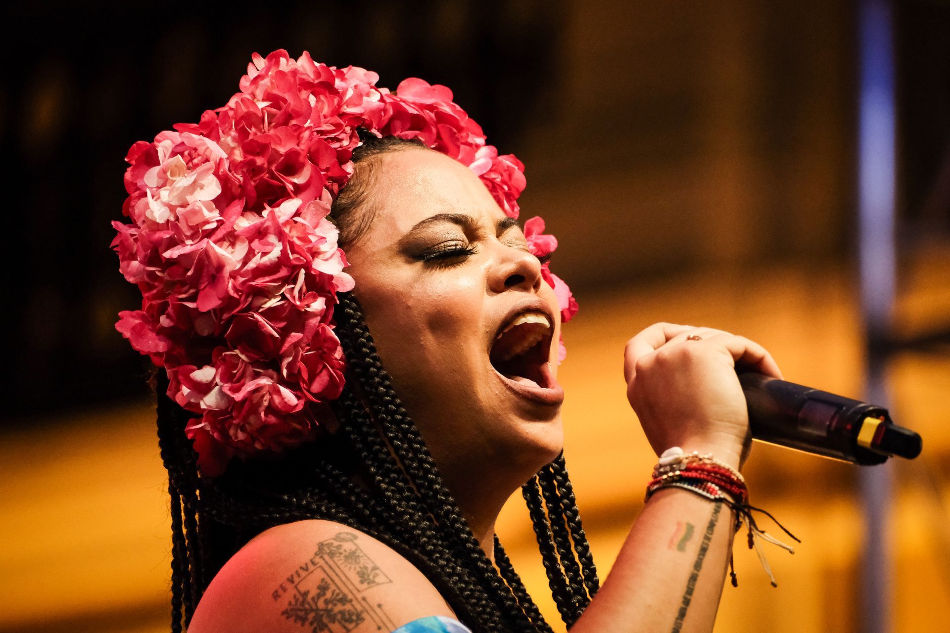 Cantante actuando en el escenario con un tocado floral rosa, cantando en un micrófono con los ojos cerrados.