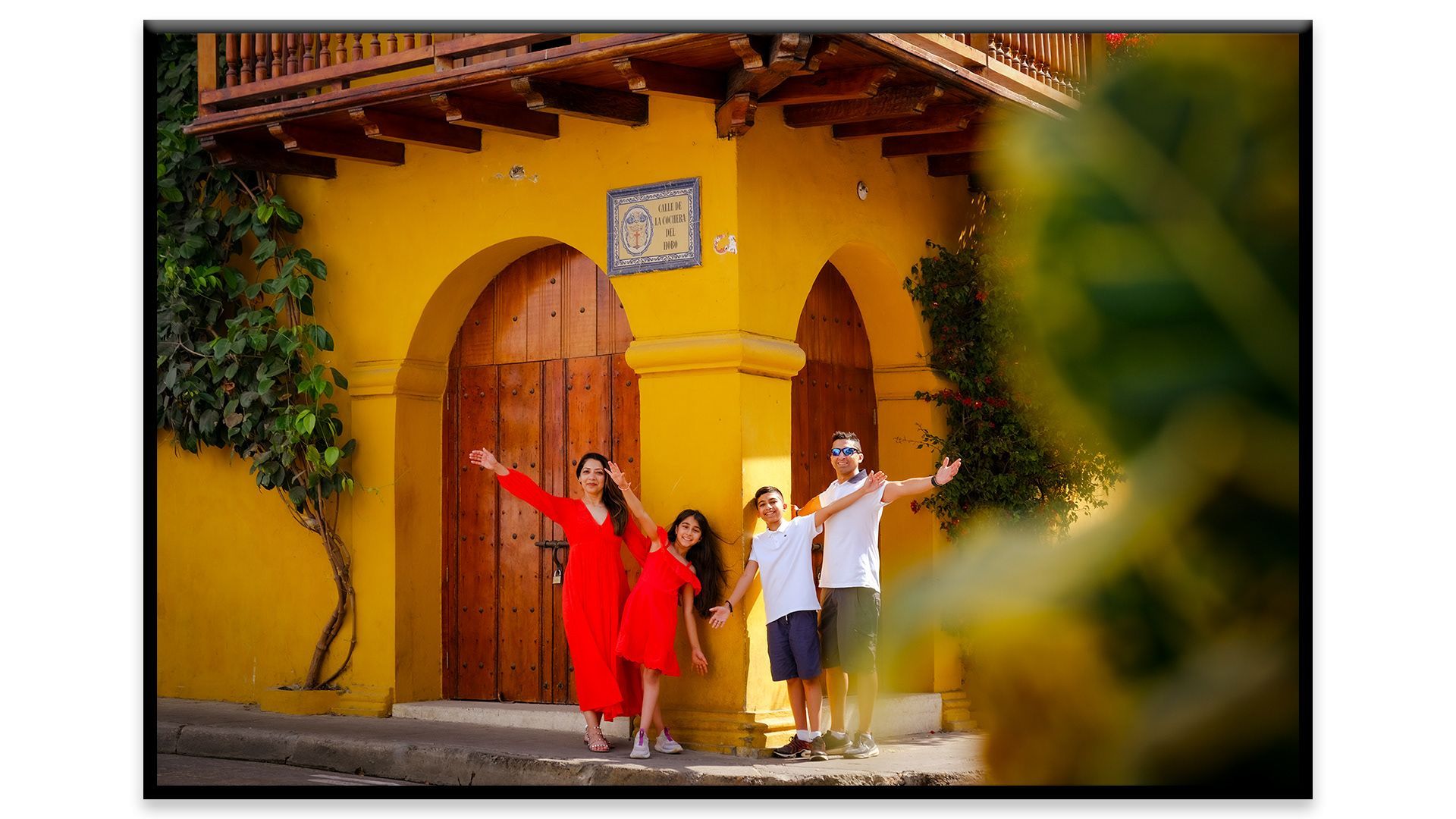 Tres personas posando frente a una puerta arqueada amarilla, una con un vestido rojo y dos con camisas blancas.