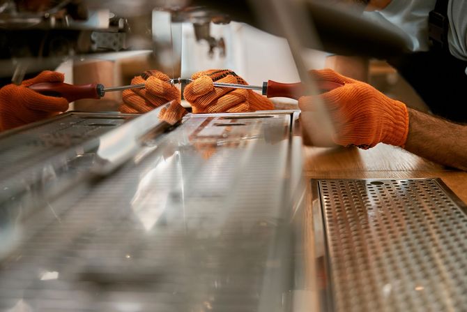 A person wearing orange gloves is working on a coffee machine.