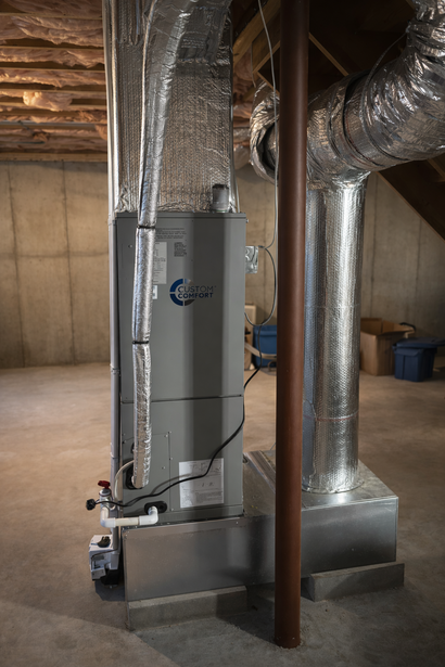 An indoor HVAC unit and metal ductwork stand in a basement with concrete walls and a floor.
